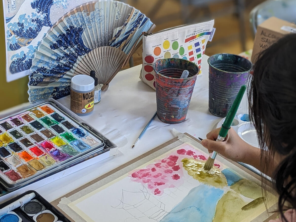 Close-up of a participant painting with watercolor supplies on the table